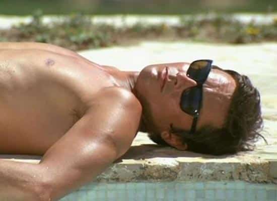 Man lying shirtless on a concrete surface, wearing black sunglasses, relaxing in the sun. highlighted image
