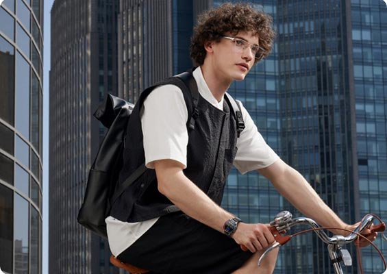 A young man carrying a backpack and wearing Huawei Eyewear 2 smart glasses on a bike in front of skyscrapers.