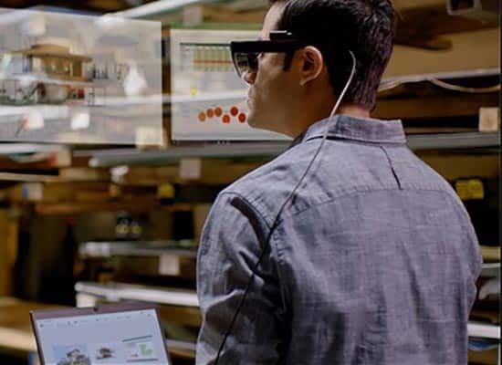 Un homme en chemise grise utilise des lunettes de réalité augmentée Lenovo ThinkReality A3 pour visualiser des données flottantes pendant qu'il travaille sur un ordinateur portable.