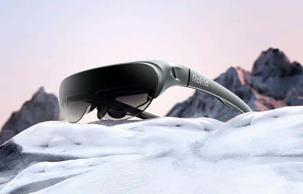 Une paire de lunettes de réalité augmentée Rokid posée sur un fond de paysage enneigé, avec une monture grise et des verres noirs translucides.