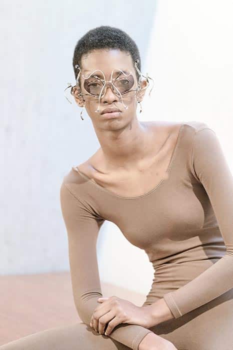 Model with unique spiral-shaped eyeglasses, posing in skin-tight skin-colored outfit, clean studio ambiance.