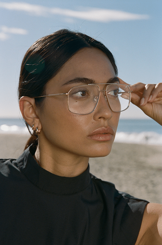 Close-up of a woman holding her transparent eyeglass frame, with the sea and blue sky in the background.