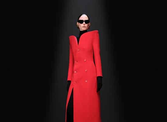 Model posing in structured red coat with opaque black sunglasses, studio lighting - featured image home page