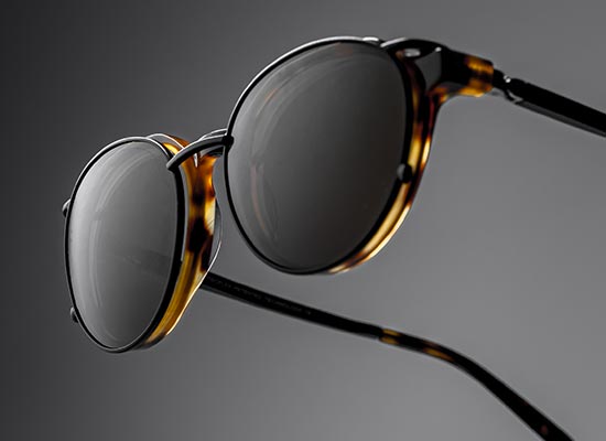 Gros plan sur des lunettes optique rondes à monture écaille avec un clip solaire, révélant le détail des verres teintés et la texture de la monture.