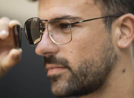 Close-up of a stylish man adjusting aviator sunglasses on his face, showing the detail of the thin metal frame.