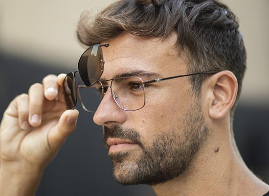 Profile portrait of a man delicately lifting his aviator sunglasses, revealing the lenses and elegant frame.