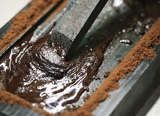 Pouring chocolate-colored material into a metal mold, close-up on the smooth and shiny texture.