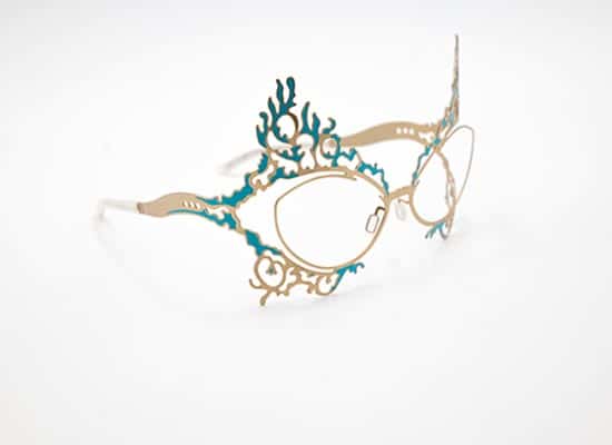 Artistic, sculptural eyeglasses with detailed gold-tone metal frames, accented with blue aquatic motifs and ornate scrollwork.
