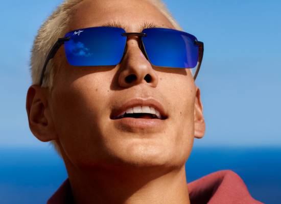 Homme avec des cheveux blonds courts portant des lunettes de soleil Maui Jim à verres bleus réfléchissants, avec un ciel bleu en arrière-plan.