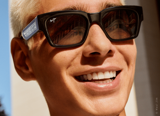 Homme souriant portant des lunettes de soleil Maui Jim noires avec des cheveux blonds platine.