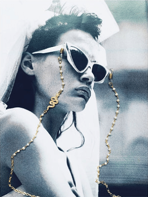 Woman wearing white sunglasses with a gold chain, posing with a veil, in black and white.