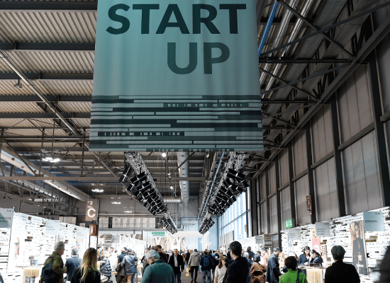 Vue d'un hall d'exposition avec des visiteurs, sous une grande enseigne "START UP" lors d'un événement professionnel.