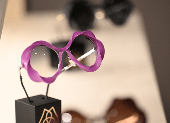 Lunettes créatives exposées avec des montures violettes au design ondulé sur un présentoir lors d'un salon optique.